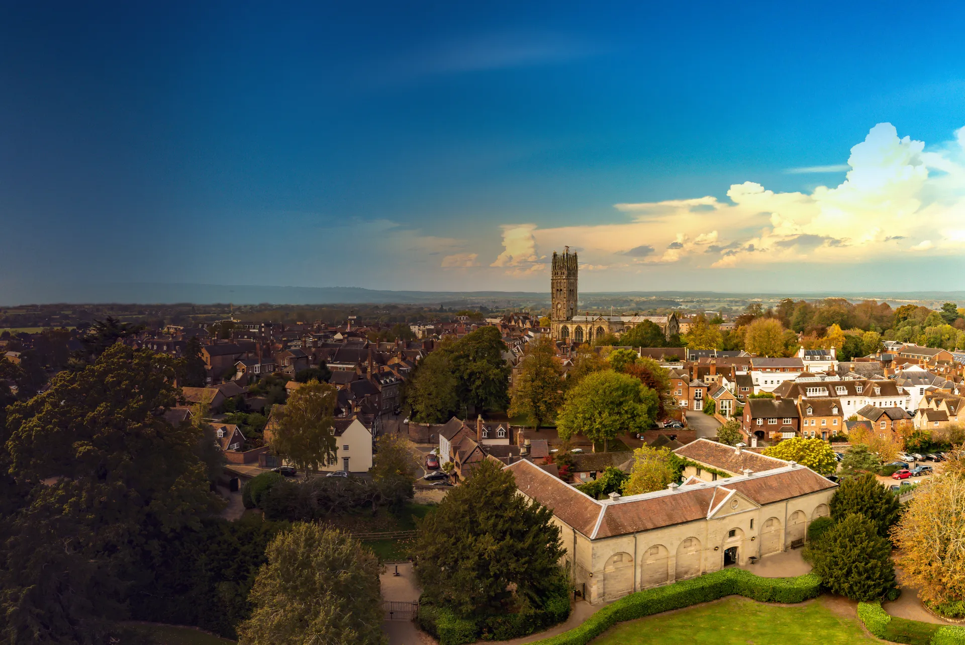 Aerial view of a historic Warwickshire town, with a church tower rising above rooftops, trees and open countryside.